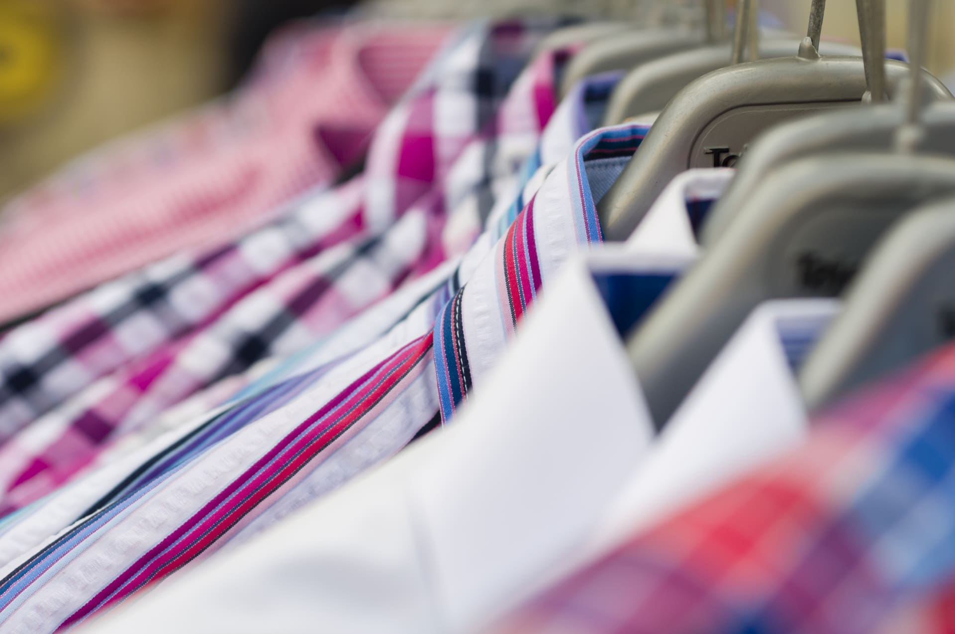 Close-up view of several colorful plaid and striped dress shirts on hangers arranged side by side on a clothing rack.